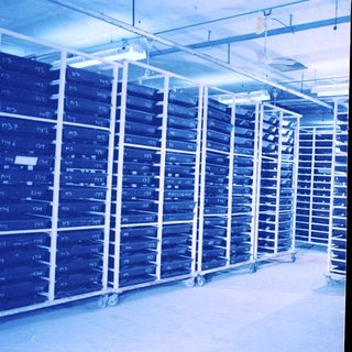 Stacked metal racks in a large, blue-lit industrial space.