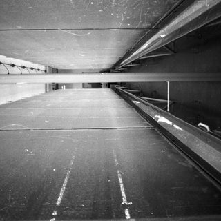 Long, narrow hallway with tracks and ceiling piping.