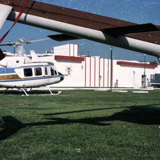 Helicopter sits on grass in front of a building.