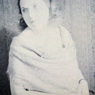 Here's a brief summary of the image: Woman in a straightjacket, possibly institutional setting.