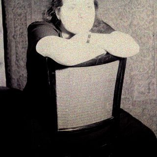 Here's a brief summary of the image: Woman seated in a chair, arms crossed, vintage photograph.
