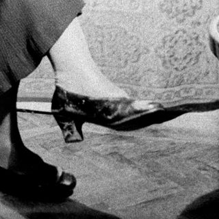 Here's a brief summary of the image: Woman seated in a chair, viewed from the knees down.