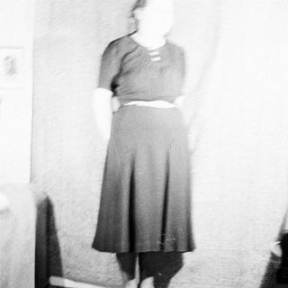 Here's a brief summary of the image: Woman in a dark skirt and sweater stands indoors.