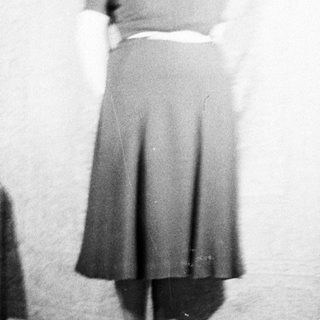 Here's a brief summary of the image: Woman in a dark skirt and sweater stands indoors.