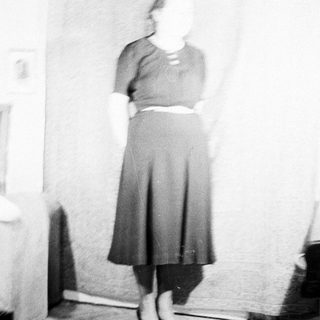 Here's a brief summary of the image: Woman in a dark skirt and sweater stands indoors.