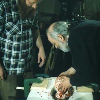 Men examining a sculpted, bloody head in a workshop.
