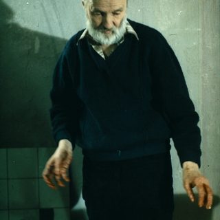 Older man stands over meat on a table.