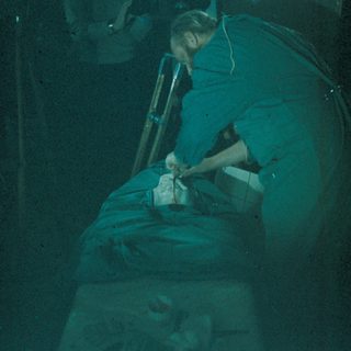 Person in green examining something on a table.