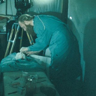 Man operating a camera in a dark, cluttered room.