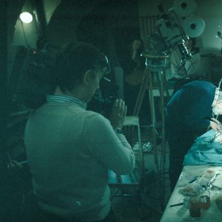 Here's a brief summary of the image: Two people working in a workshop, surrounded by tools.