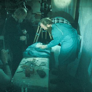 Men examining a body on a table in a dark room.