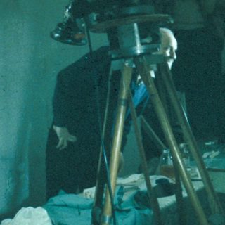 Film crew working in a dimly lit, clinical setting.