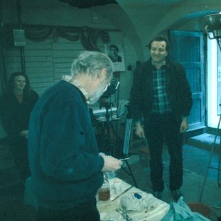 Man sculpts, two people observe in a workshop setting.