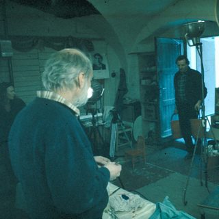 Man working in a cluttered, dimly lit room with equipment.