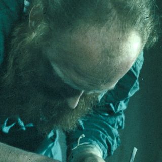 Man examines a bust with a tool, likely an artist.