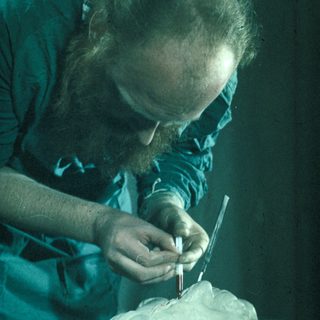 Man examines a bust with a tool, likely an artist.