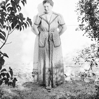 Woman stands outdoors near foliage and a wall.