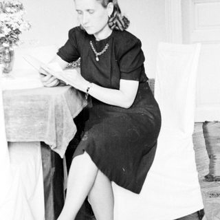 Woman seated, reading at a table in a room.