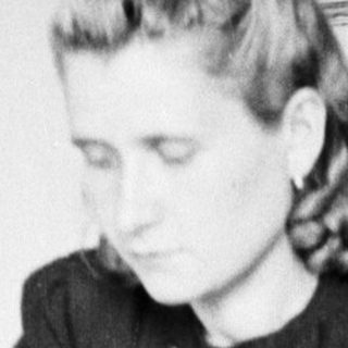 Woman seated, reading at a table in a room.