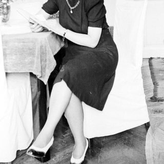 Woman seated, reading at a table in a room.