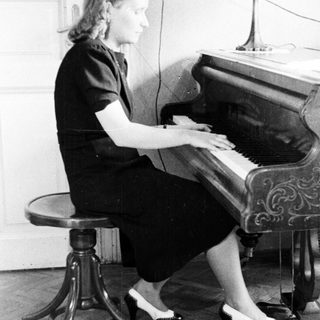 Woman sits at a piano playing in a room.