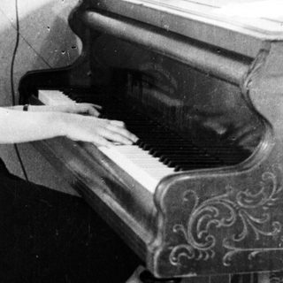 Woman sits at a piano playing in a room.