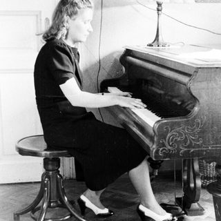 Woman sits at a piano playing in a room.