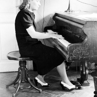 Woman sits at a piano playing in a room.