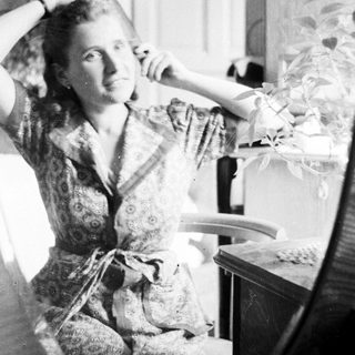 Woman seated, hands raised, in a patterned dress.