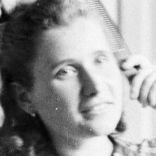 Woman seated, hands raised, in a patterned dress.