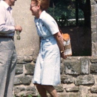 Couple stands near stone pillars and a plaque.