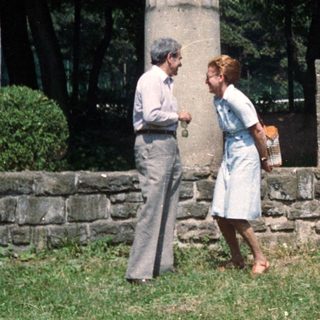 Couple stands near stone pillars and a plaque.