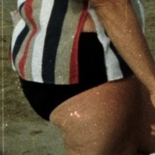 Woman stands on a beach with a windsurfer in the distance.