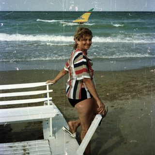 Woman stands on a beach with a windsurfer in the distance.