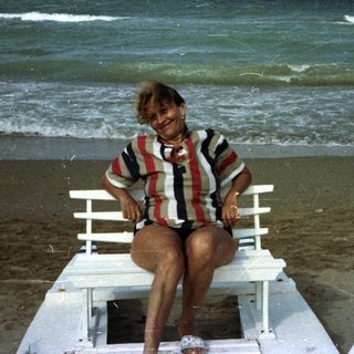 Woman sits on a beach chair by the ocean.