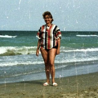 Woman stands on beach, children play in the ocean.