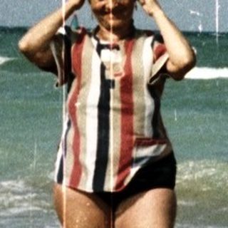 Woman stands on a sandy beach with ocean backdrop.