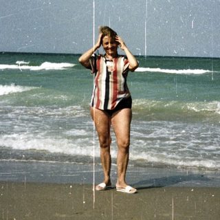 Woman stands on a sandy beach with ocean backdrop.