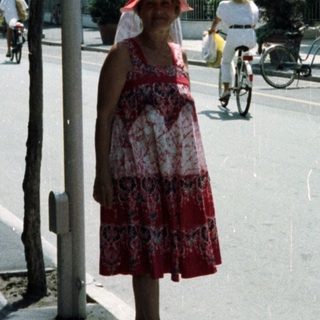 Woman stands near a storefront with cyclists in the background.