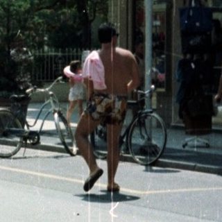 Woman stands near a storefront with cyclists in the background.