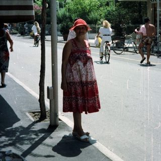 Woman stands near a storefront with cyclists in the background.