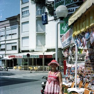 Woman stands on street near restaurant with tables.
