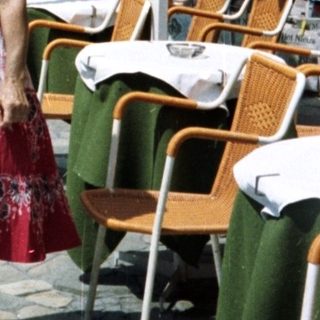 Woman stands on street near restaurant with tables.
