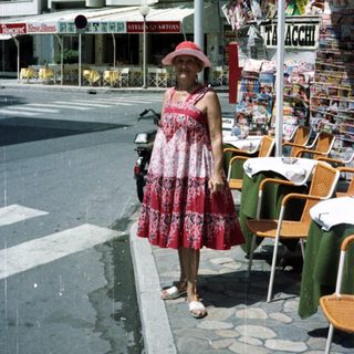 Woman stands on street near restaurant with tables.