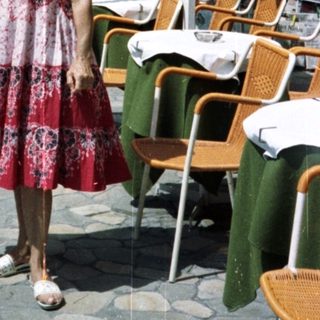 Woman stands on street near restaurant with tables.