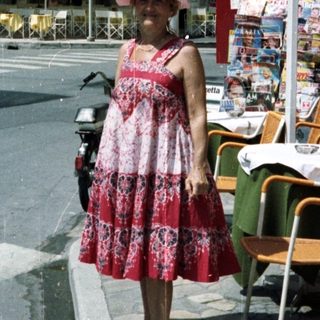 Woman stands on street near restaurant with tables.