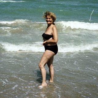 Woman stands in shallow water on a sunny beach.