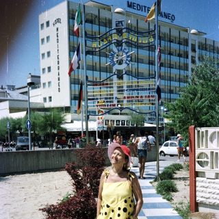 Woman stands on a pathway near a hotel and beach.