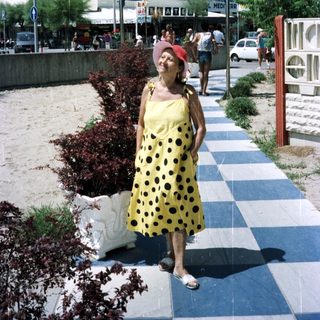 Woman stands on a pathway near a hotel and beach.