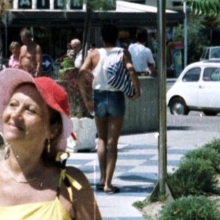 Woman stands on a pathway near a hotel and beach.